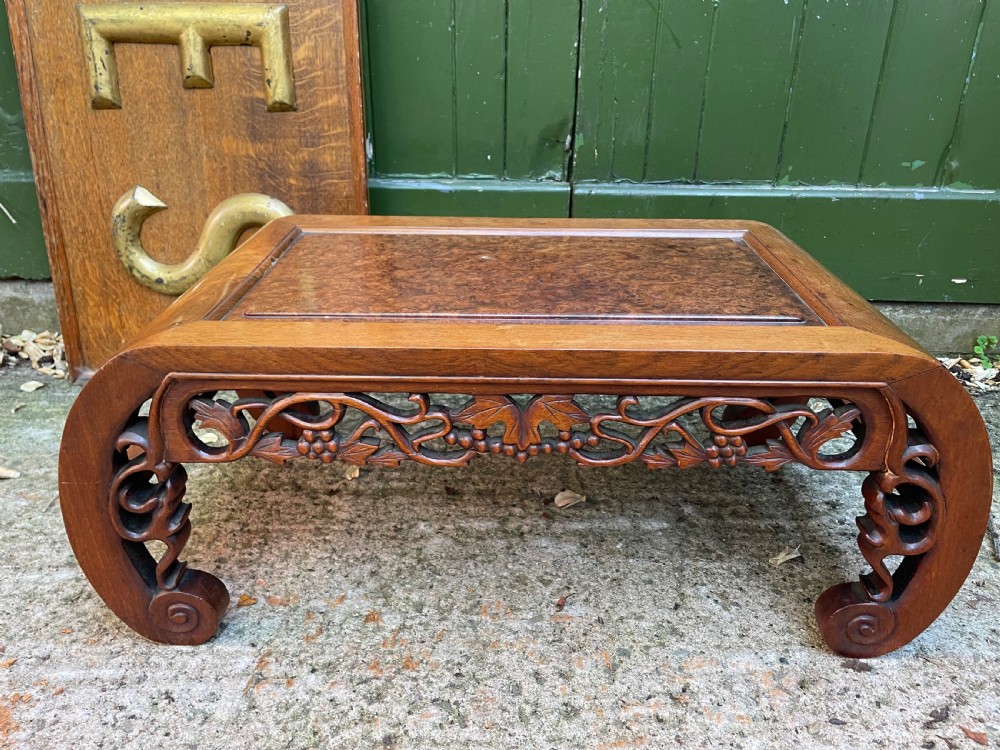 A low carved dark hardwood Chinese Kang table featuring scroll feet and a pierced floral apron.