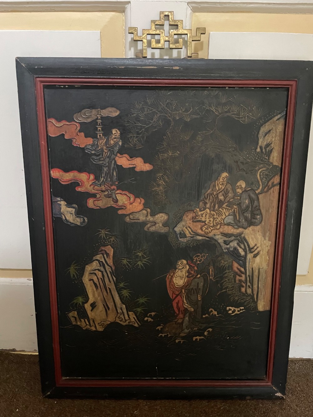 A set of four rectangular black lacquer panels framed in dark wood with red inner borders, depicting carved Chinese figurative scenes in landscape settings. View IV