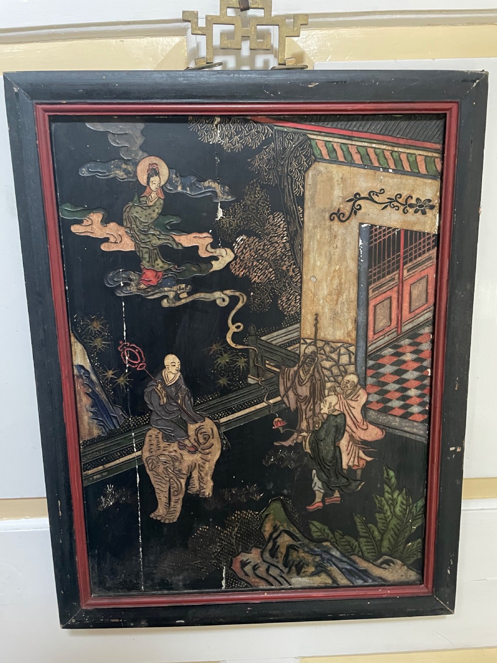 A set of four rectangular black lacquer panels framed in dark wood with red inner borders, depicting carved Chinese figurative scenes in landscape settings. View VI