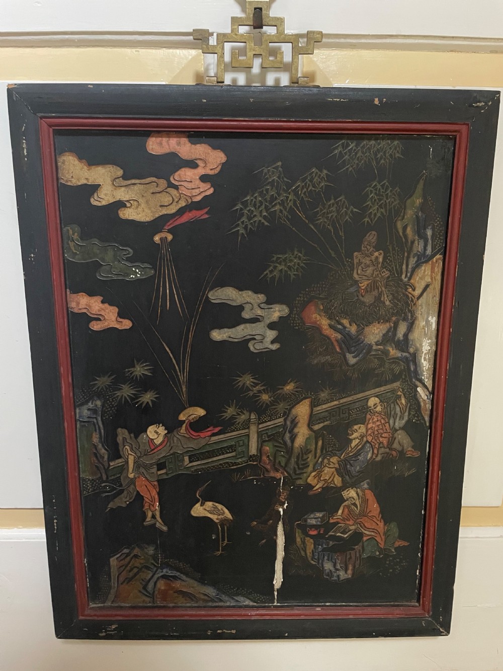 A set of four rectangular black lacquer panels framed in dark wood with red inner borders, depicting carved Chinese figurative scenes in landscape settings. View VII