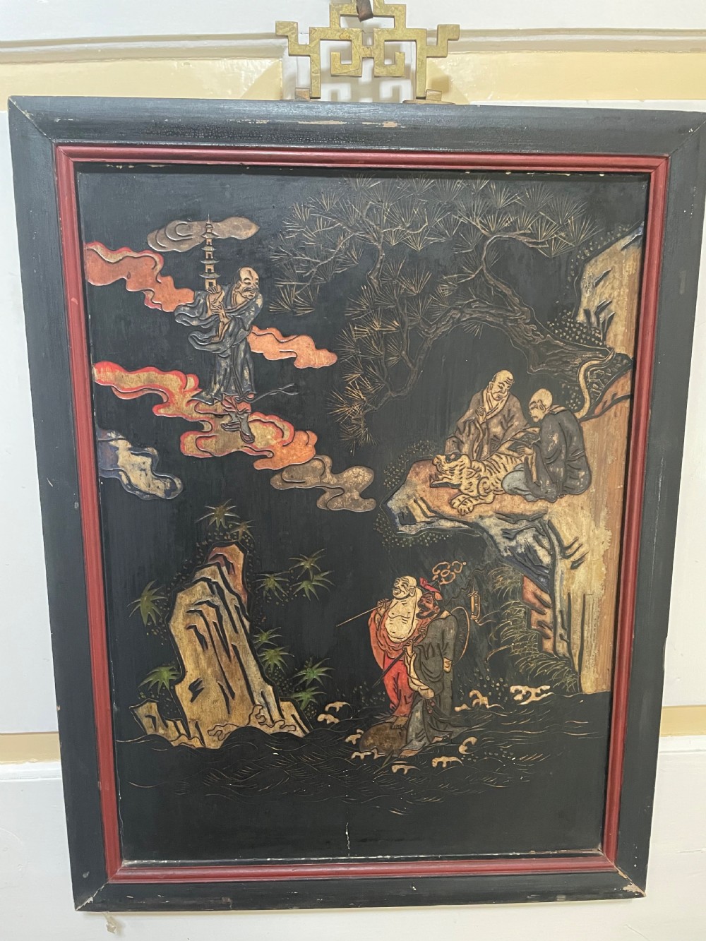 A set of four rectangular black lacquer panels framed in dark wood with red inner borders, depicting carved Chinese figurative scenes in landscape settings. View VIII