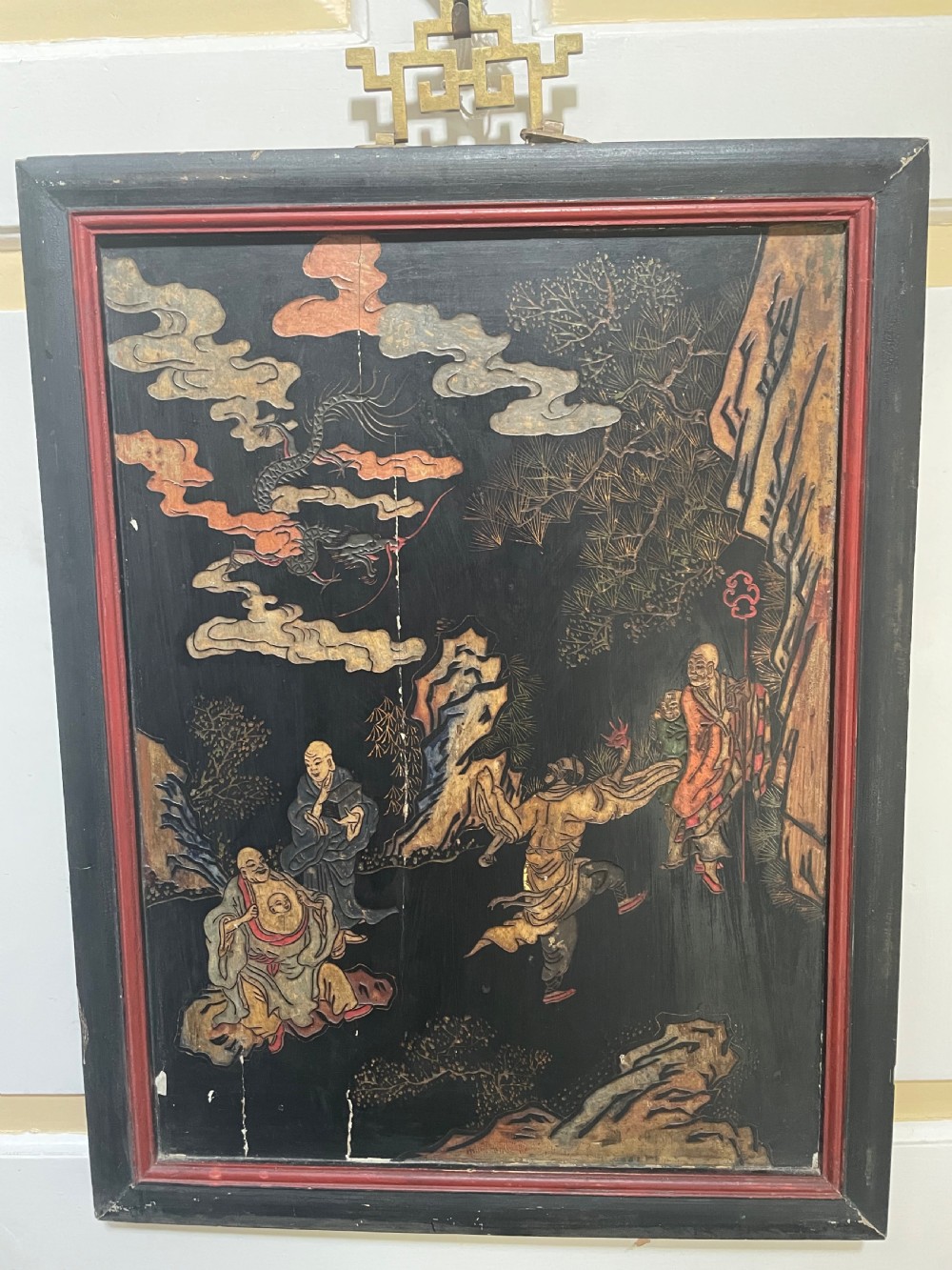 A set of four rectangular black lacquer panels framed in dark wood with red inner borders, depicting carved Chinese figurative scenes in landscape settings. View IX