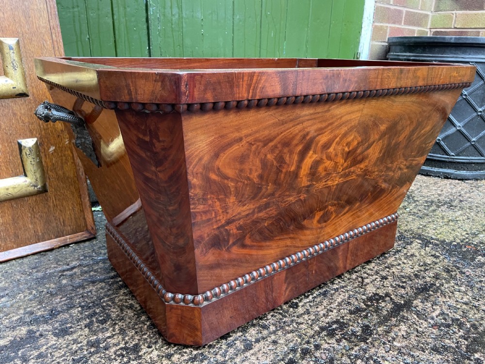 A George IV open mahogany wine cooler of classical sarcophagus form featuring flame mahogany veneer panels and carved bead moulding. View III