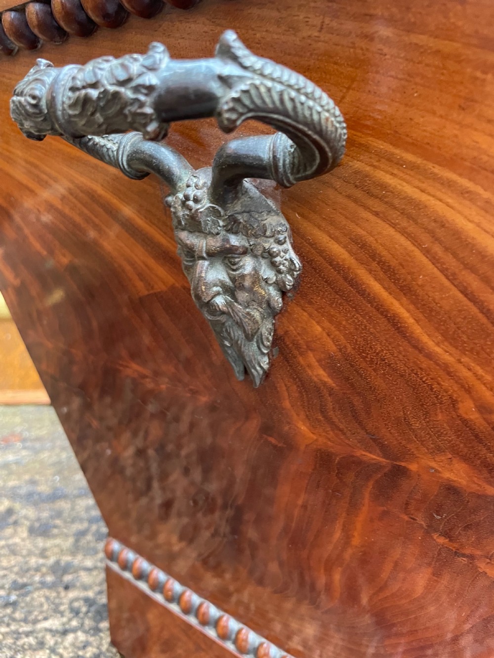 A George IV open mahogany wine cooler of classical sarcophagus form featuring flame mahogany veneer panels and carved bead moulding. View V