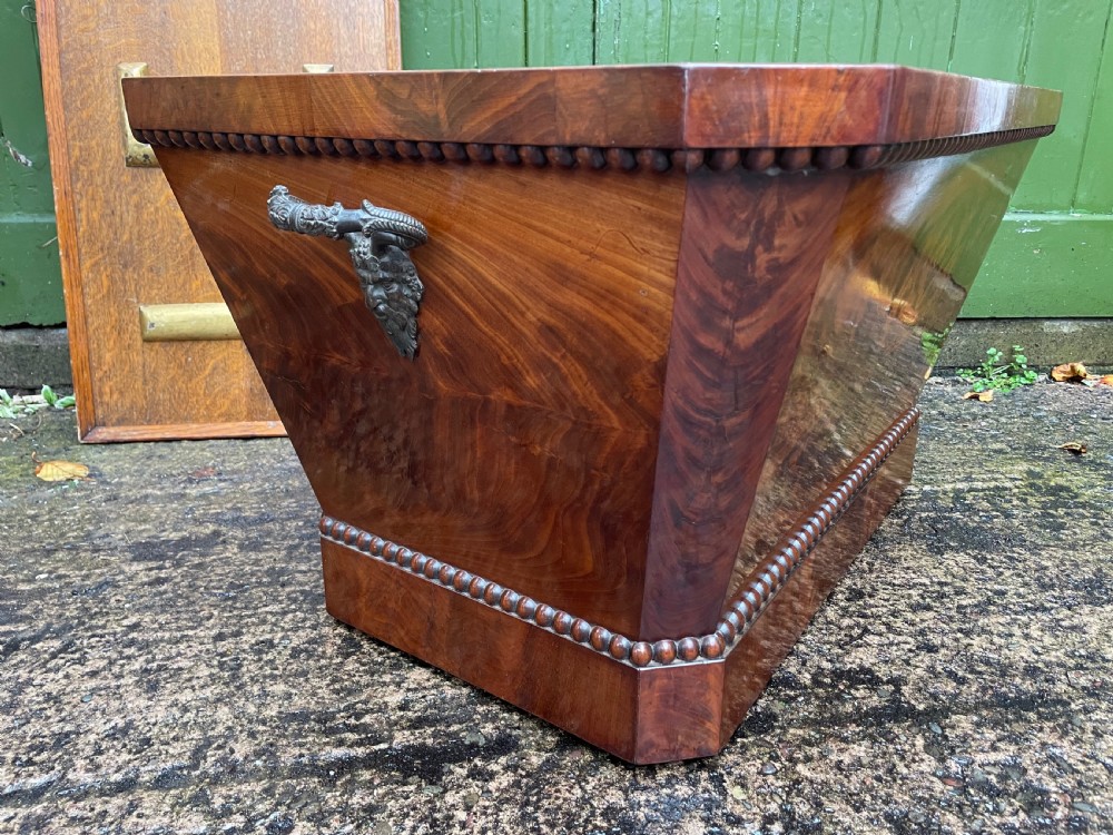A George IV open mahogany wine cooler of classical sarcophagus form featuring flame mahogany veneer panels and carved bead moulding. View VI