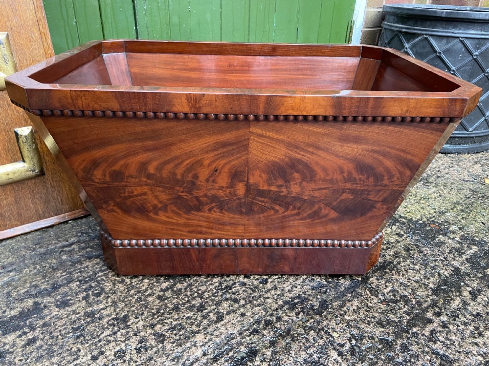 A George IV open mahogany wine cooler of classical sarcophagus form featuring flame mahogany veneer panels and carved bead moulding. View VIII