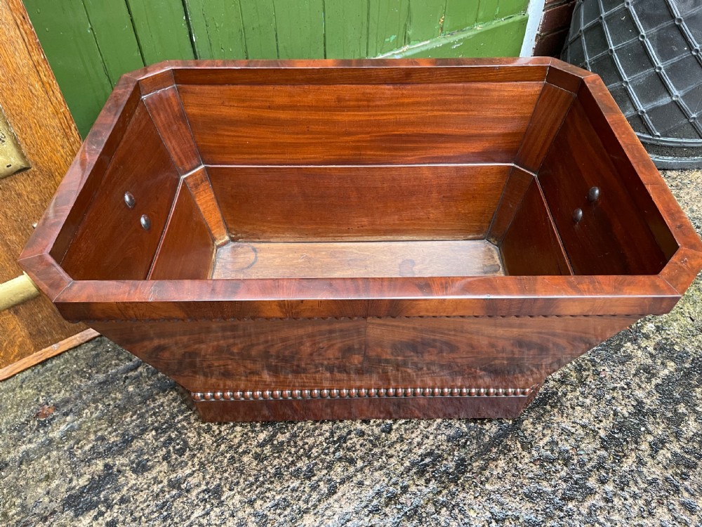 A George IV open mahogany wine cooler of classical sarcophagus form featuring flame mahogany veneer panels and carved bead moulding. View IX