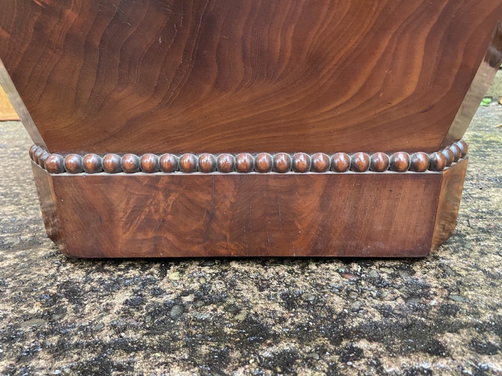 A George IV open mahogany wine cooler of classical sarcophagus form featuring flame mahogany veneer panels and carved bead moulding. View XIX