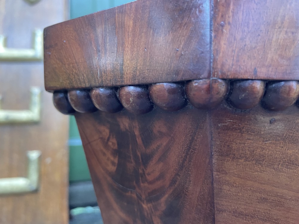 A George IV open mahogany wine cooler of classical sarcophagus form featuring flame mahogany veneer panels and carved bead moulding. View XX