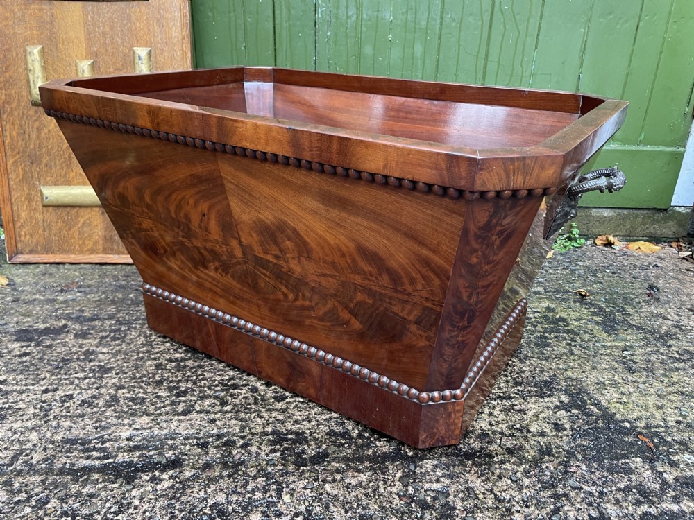 A George IV open mahogany wine cooler of classical sarcophagus form featuring flame mahogany veneer panels and carved bead moulding. View XXII