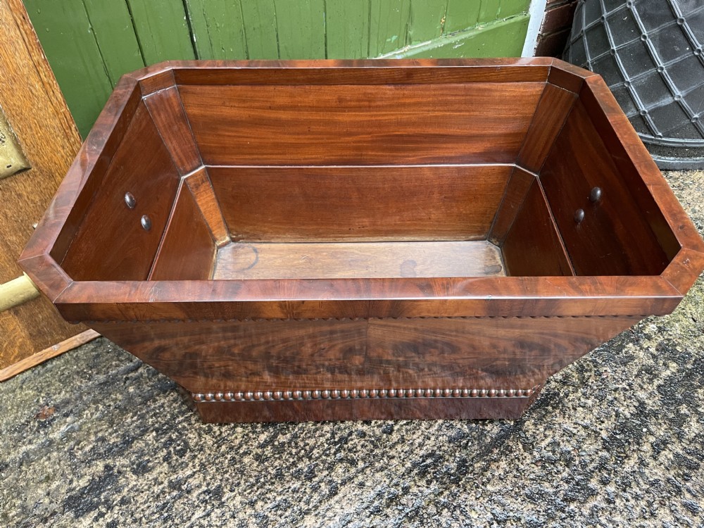 A George IV open mahogany wine cooler of classical sarcophagus form featuring flame mahogany veneer panels and carved bead moulding. View XXV