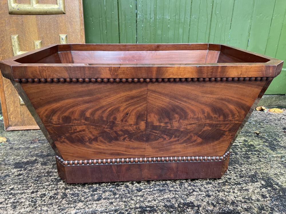 A George IV open mahogany wine cooler of classical sarcophagus form featuring flame mahogany veneer panels and carved bead moulding. View XXVI