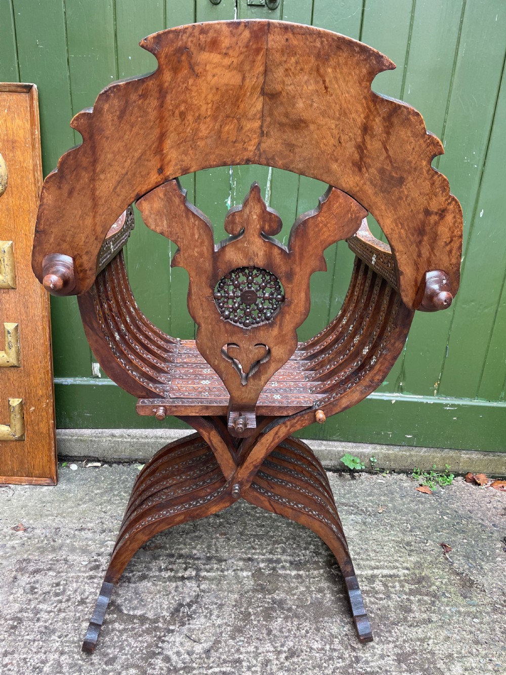 A Syrian dark walnut X-frame armchair featuring intricate Arabic calligraphy carvings and geometric mother-of-pearl shell inlay throughout. View X