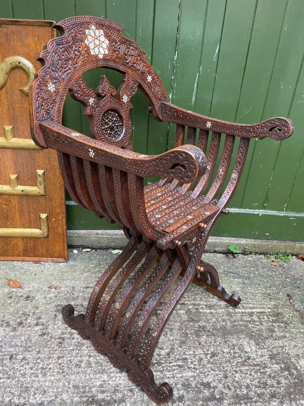 A Syrian dark walnut X-frame armchair featuring intricate Arabic calligraphy carvings and geometric mother-of-pearl shell inlay throughout. View XII