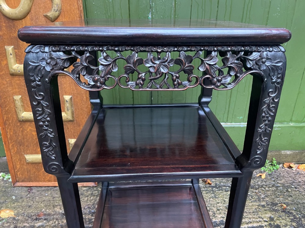 A late nineteenth-century Chinese square dark hardwood two-tier side table featuring intricately carved floral openwork aprons and lower shelf tiers. View V