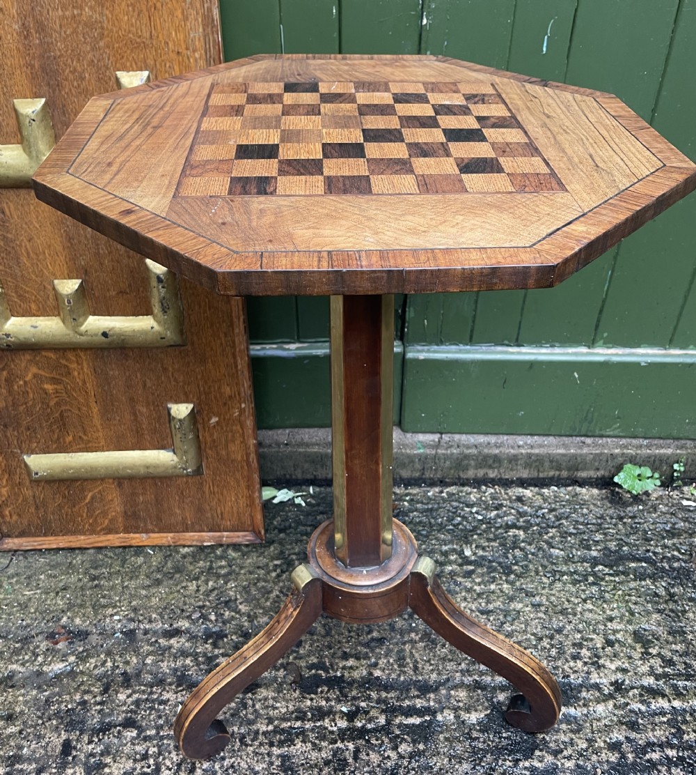 An early nineteenth-century Regency octagonal rosewood games table with a chequerboard inlaid top, brass mounts, and a tripod base. View XV