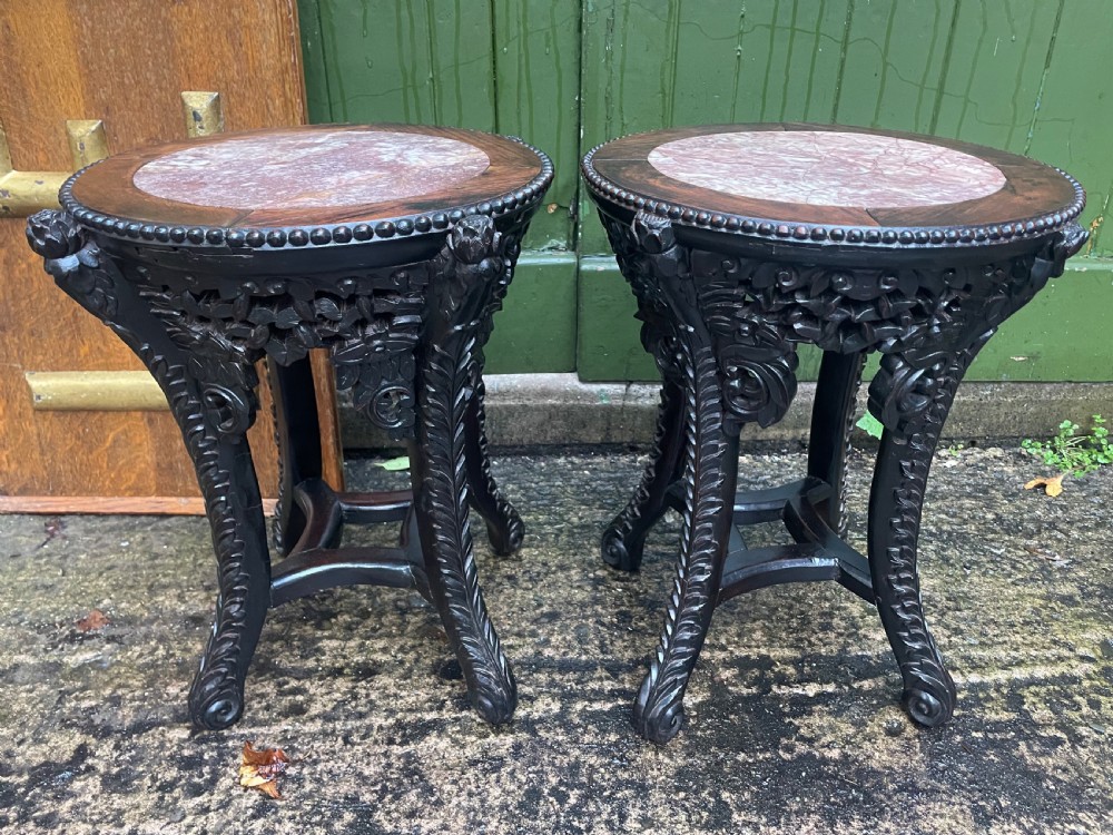 A pair of circular late nineteenth-century Chinese hardwood stands featuring inset pinkish rouge marble tops and intricately carved aprons and legs.