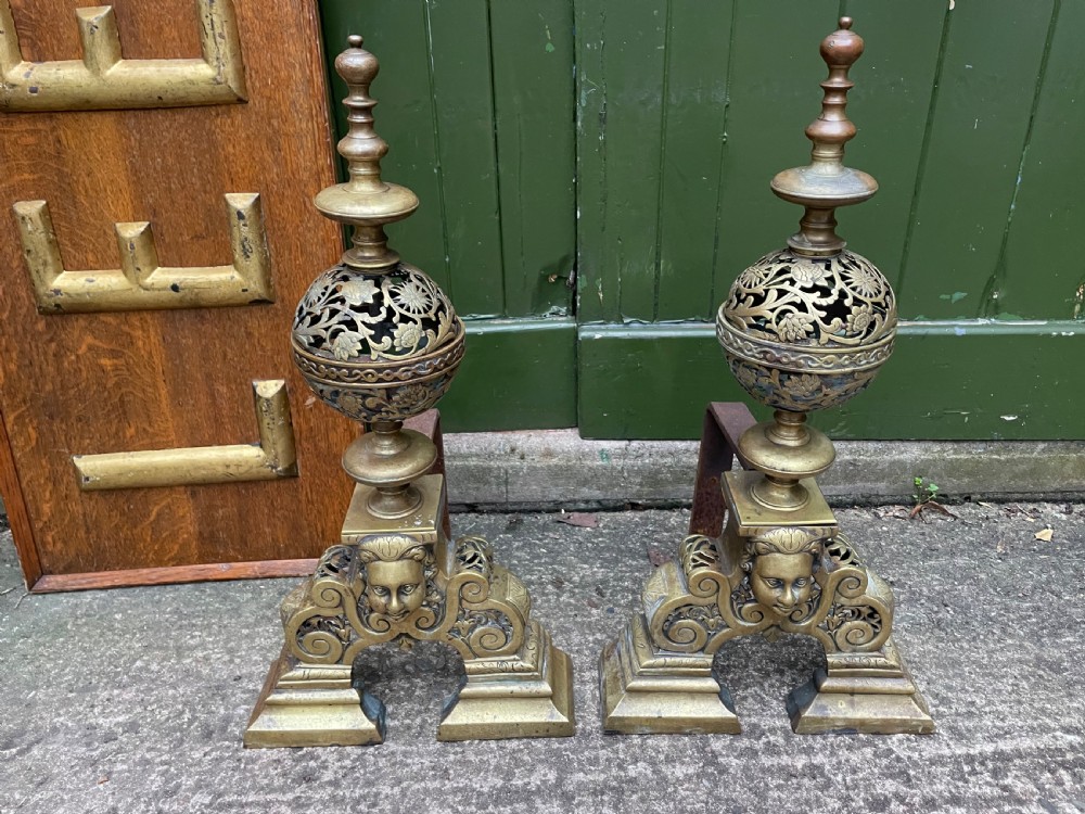 A pair of 19th-century Baroque revival brass andirons featuring mascaron face motifs, openwork spherical finials, and scrolled bases. View II