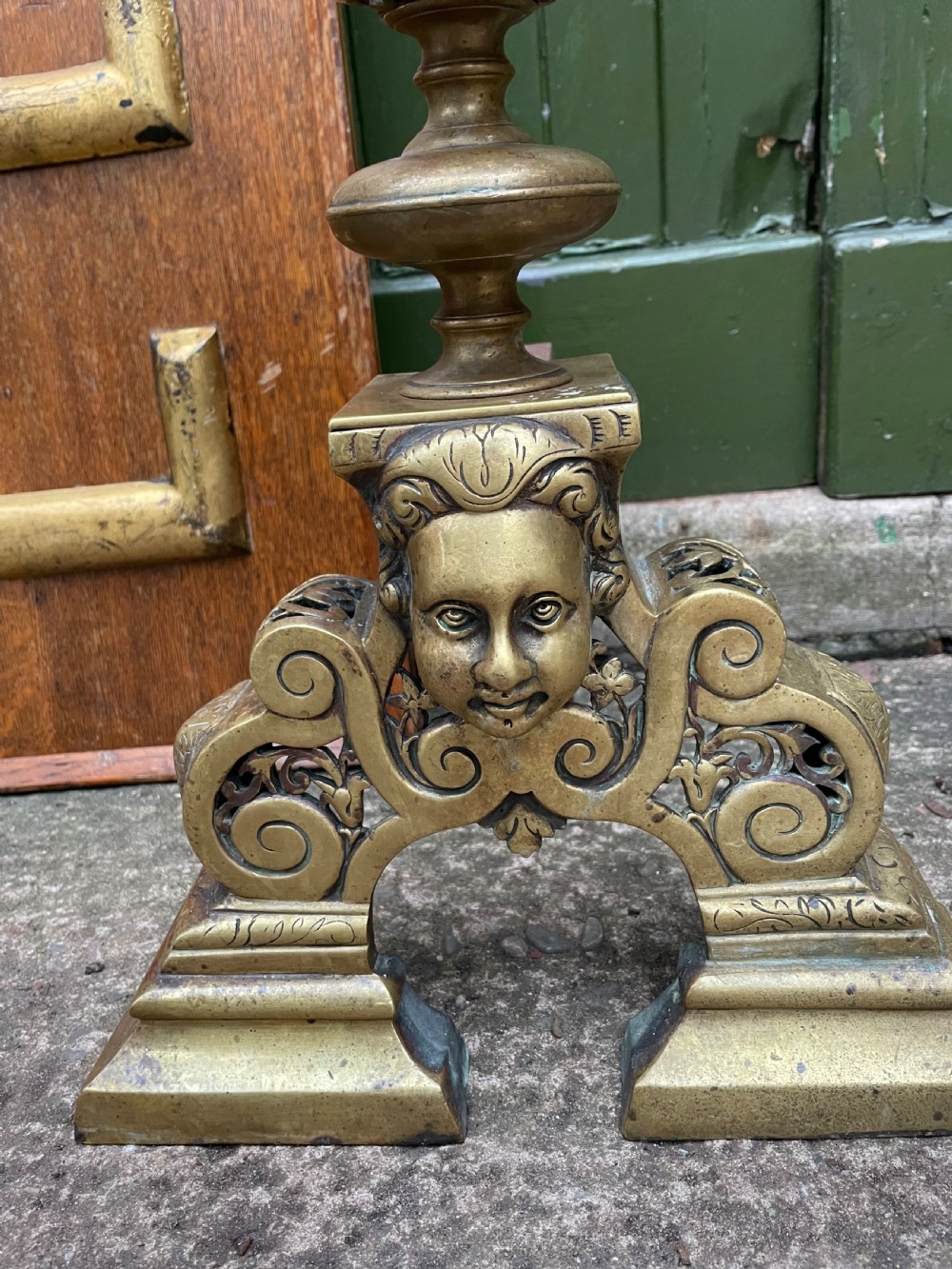 A pair of 19th-century Baroque revival brass andirons featuring mascaron face motifs, openwork spherical finials, and scrolled bases. View V