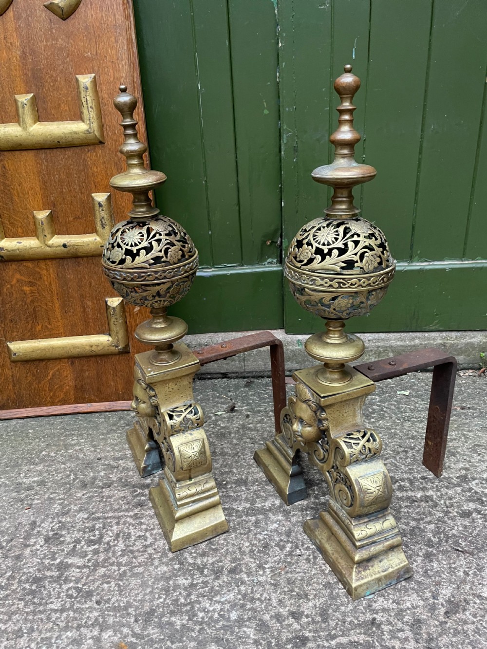 A pair of 19th-century Baroque revival brass andirons featuring mascaron face motifs, openwork spherical finials, and scrolled bases. View VI