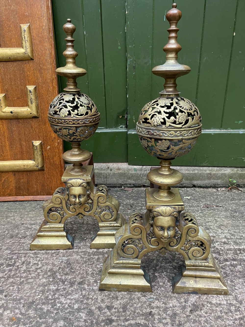 A pair of 19th-century Baroque revival brass andirons featuring mascaron face motifs, openwork spherical finials, and scrolled bases. View VII