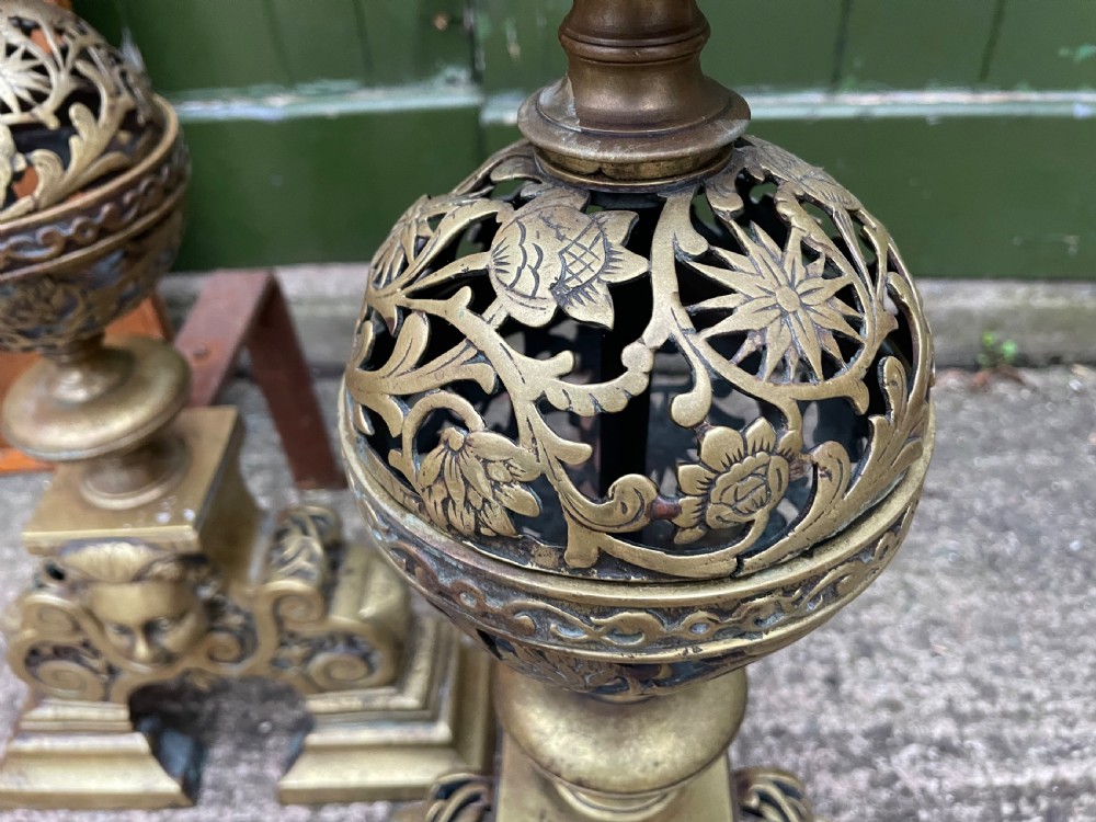 A pair of 19th-century Baroque revival brass andirons featuring mascaron face motifs, openwork spherical finials, and scrolled bases. View IX