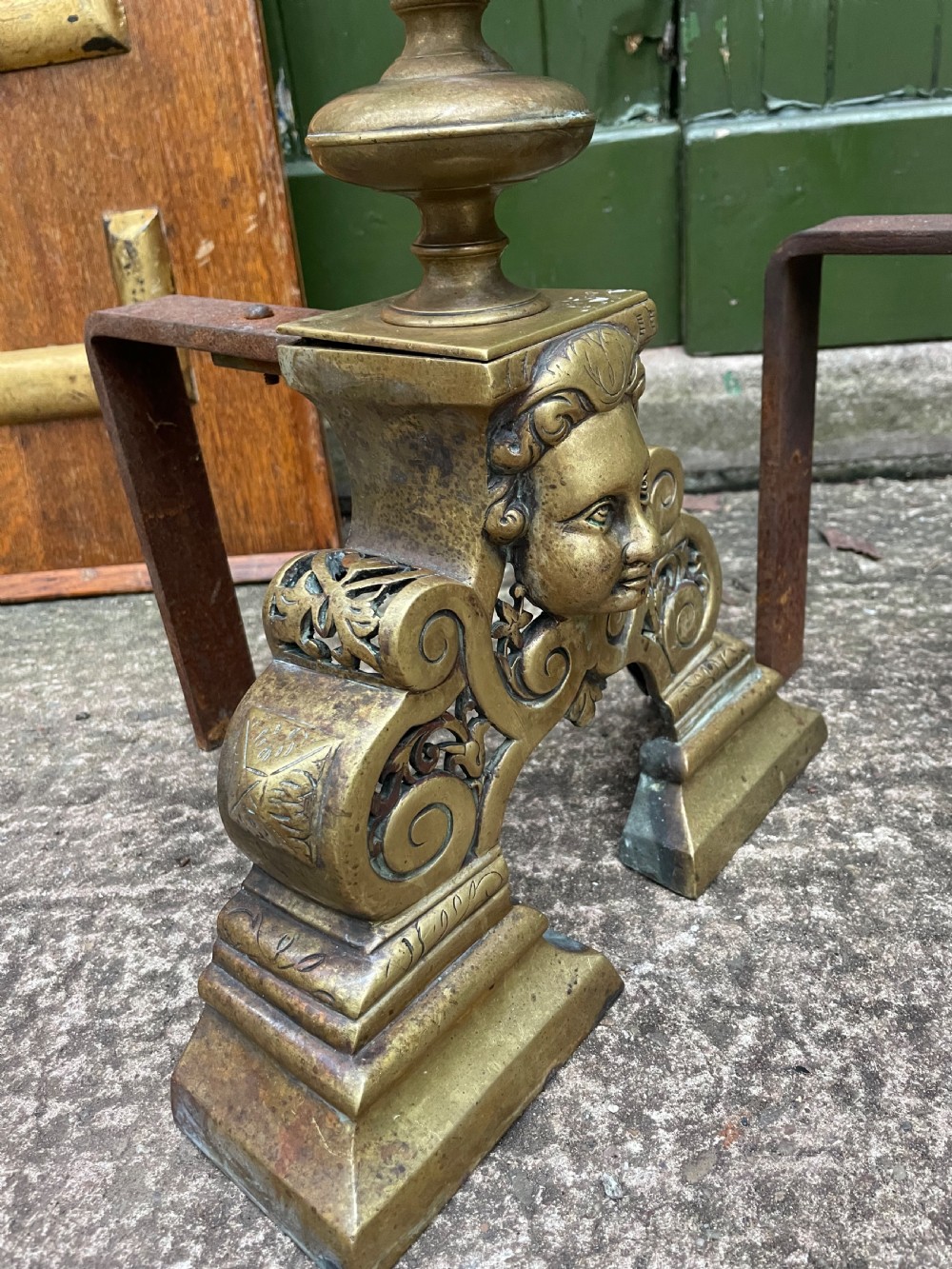A pair of 19th-century Baroque revival brass andirons featuring mascaron face motifs, openwork spherical finials, and scrolled bases. View XII