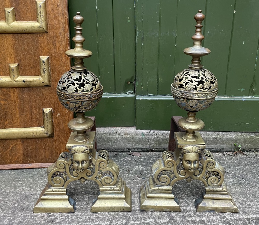 A pair of 19th-century Baroque revival brass andirons featuring mascaron face motifs, openwork spherical finials, and scrolled bases.