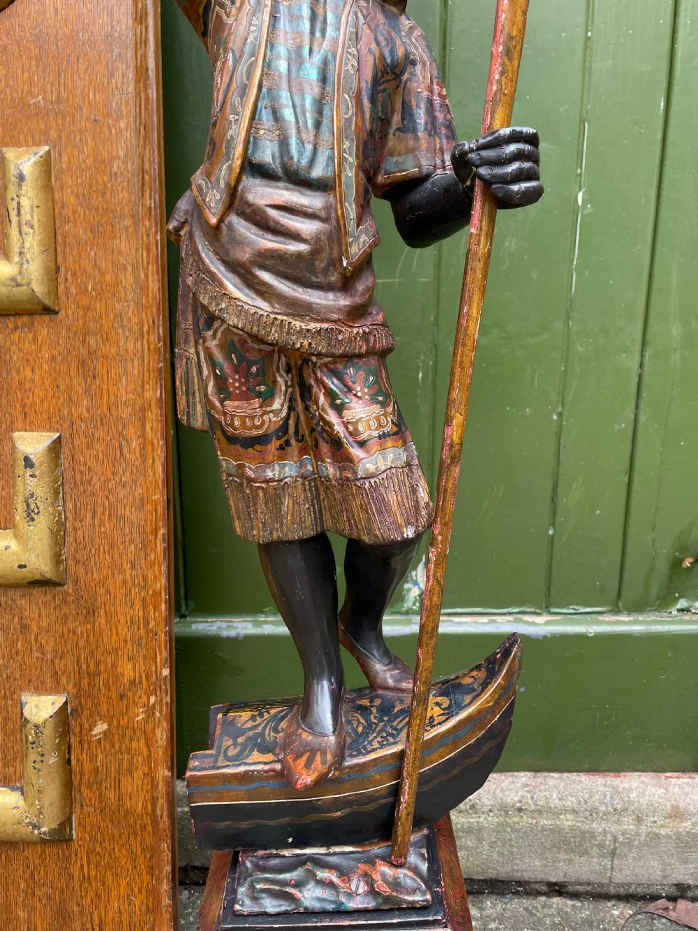 A late 19th-century Italian Venetian carved wood polychrome figure of a gondolier standing on a boat base atop a plinth, holding an oar and raised tray. View V