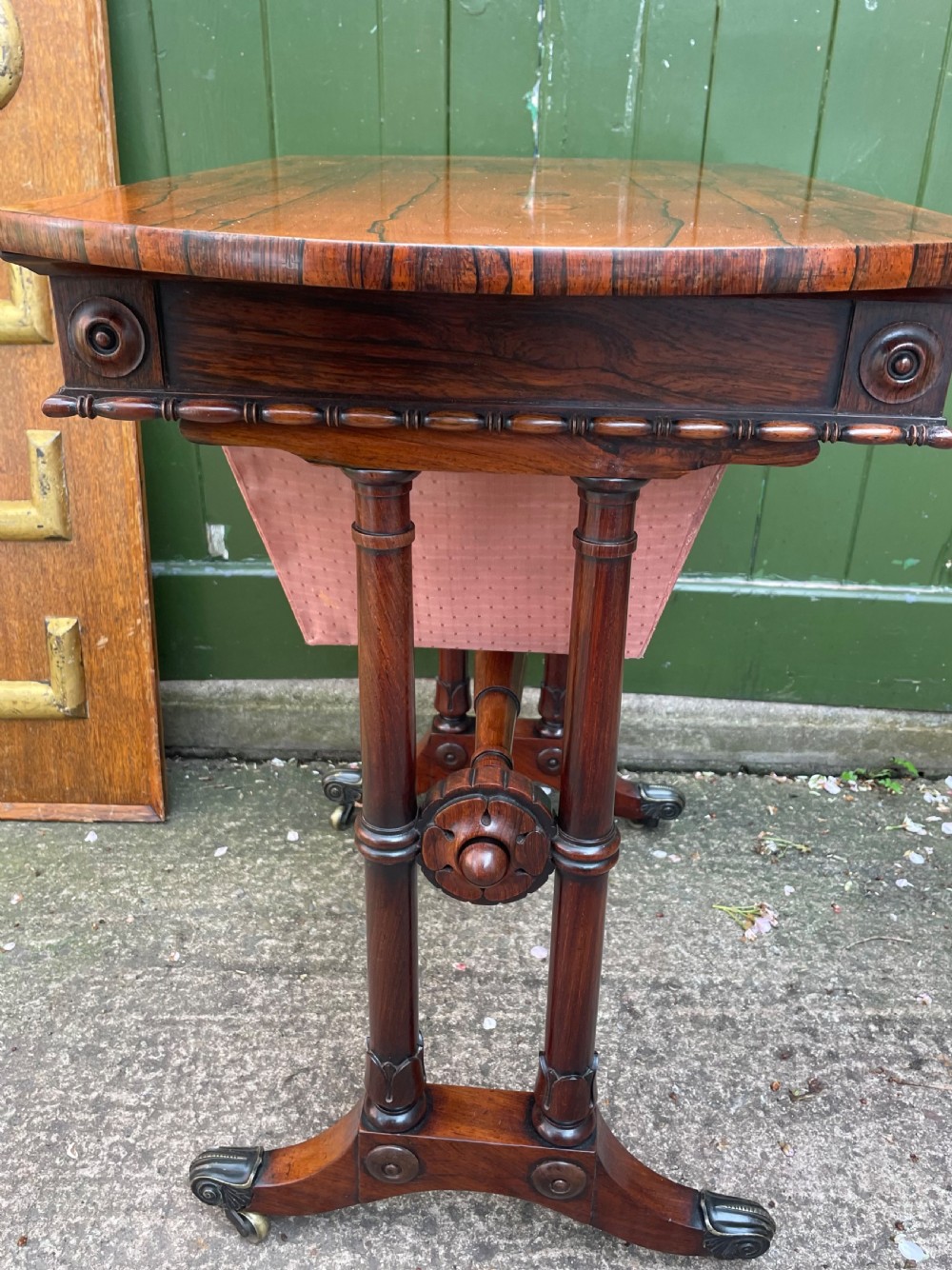 An early 19th-century George IV figured rosewood work table featuring a smooth polished top, single drawer, fabric work basket, turned twin-column supports, and brass castors. View IX