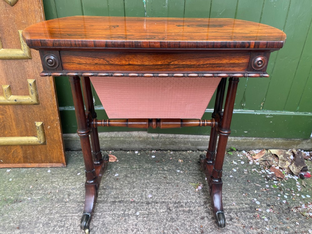 An early 19th-century George IV figured rosewood work table featuring a smooth polished top, single drawer, fabric work basket, turned twin-column supports, and brass castors. View XIII