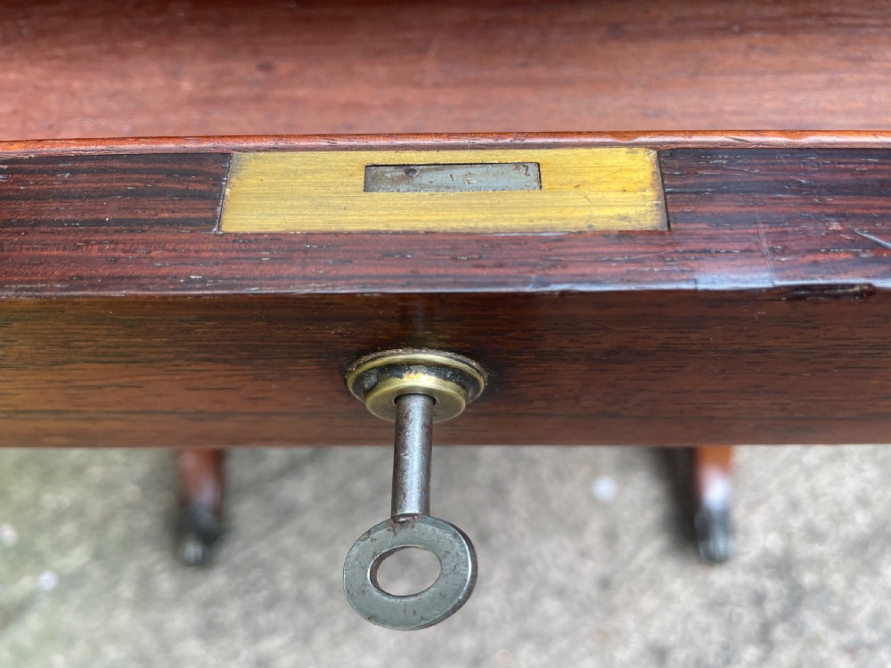 An early 19th-century George IV figured rosewood work table featuring a smooth polished top, single drawer, fabric work basket, turned twin-column supports, and brass castors. View XVIII