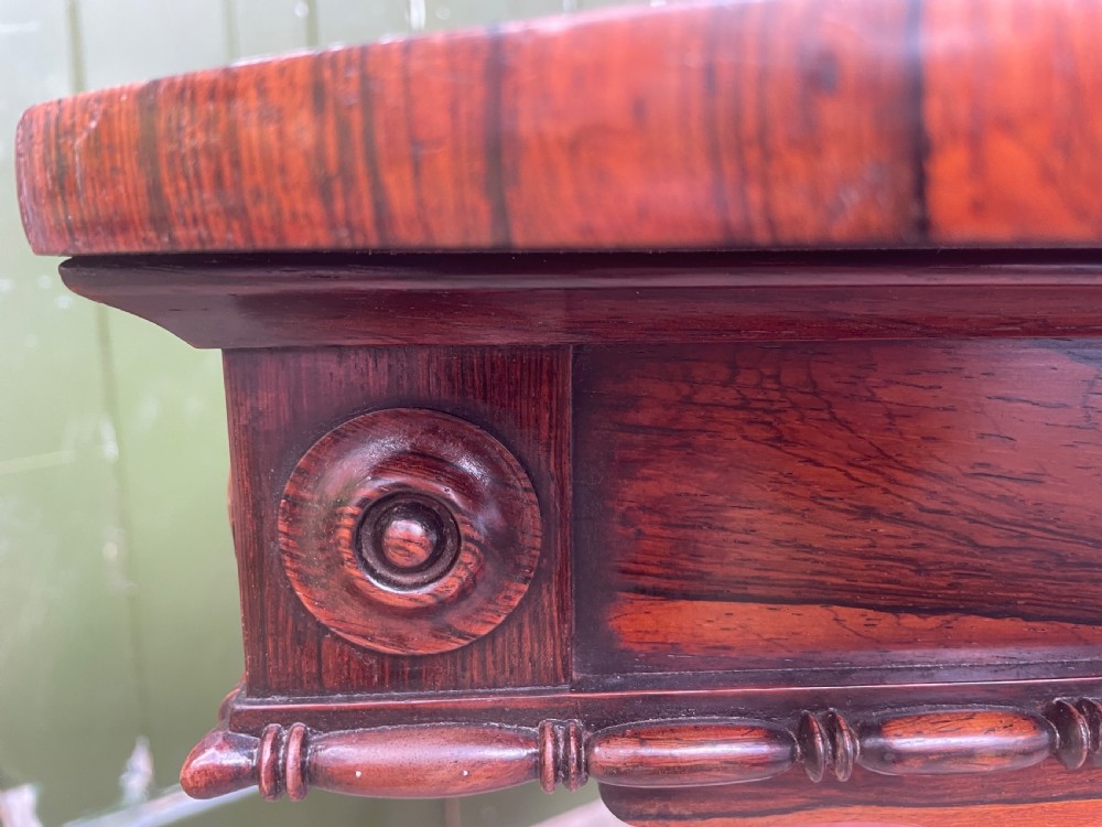 An early 19th-century George IV figured rosewood work table featuring a smooth polished top, single drawer, fabric work basket, turned twin-column supports, and brass castors. View XXVI