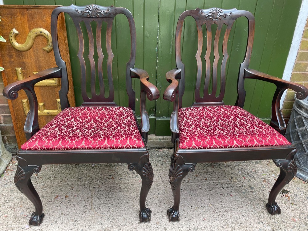 A pair of 19th-century mahogany open armchairs featuring carved shell cresting, pierced vertical splats, patterned red velvet seats, and cabriole legs with claw and ball feet.