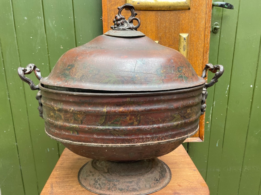 An early nineteenth-century round japanned tinware wine cooler with a domed lid, pedestal base, twin loop handles, and faded painted floral motifs.