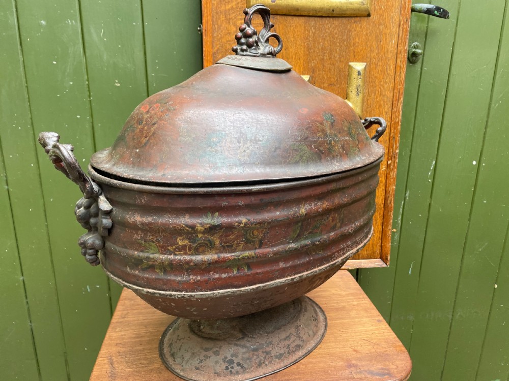 An early nineteenth-century round japanned tinware wine cooler with a domed lid, pedestal base, twin loop handles, and faded painted floral motifs. View II