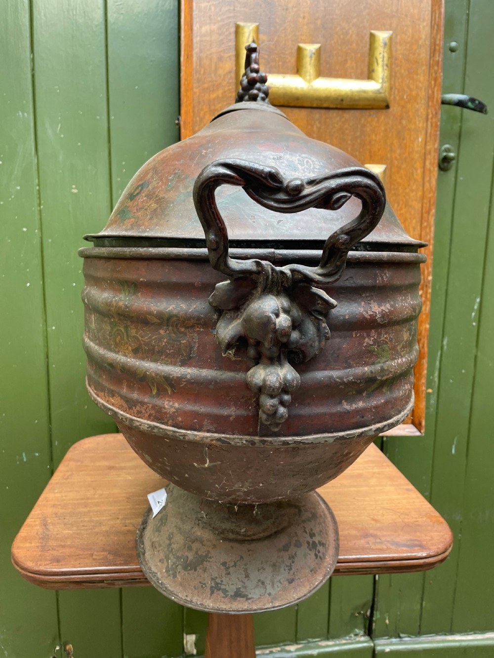 An early nineteenth-century round japanned tinware wine cooler with a domed lid, pedestal base, twin loop handles, and faded painted floral motifs. View III