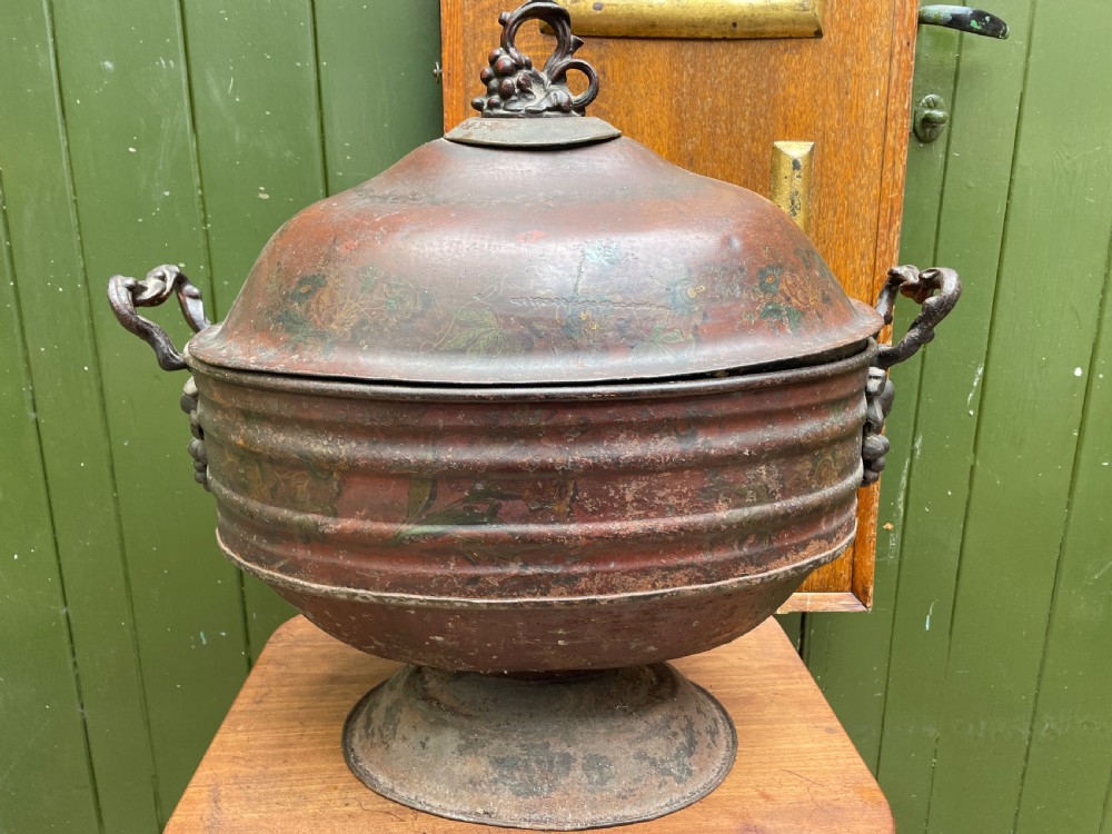 An early nineteenth-century round japanned tinware wine cooler with a domed lid, pedestal base, twin loop handles, and faded painted floral motifs. View XV