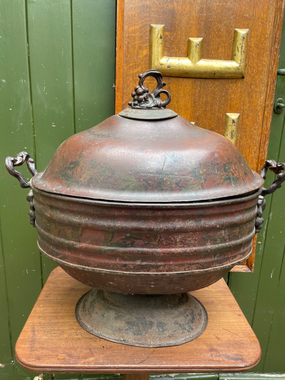 An early nineteenth-century round japanned tinware wine cooler with a domed lid, pedestal base, twin loop handles, and faded painted floral motifs. View XVII