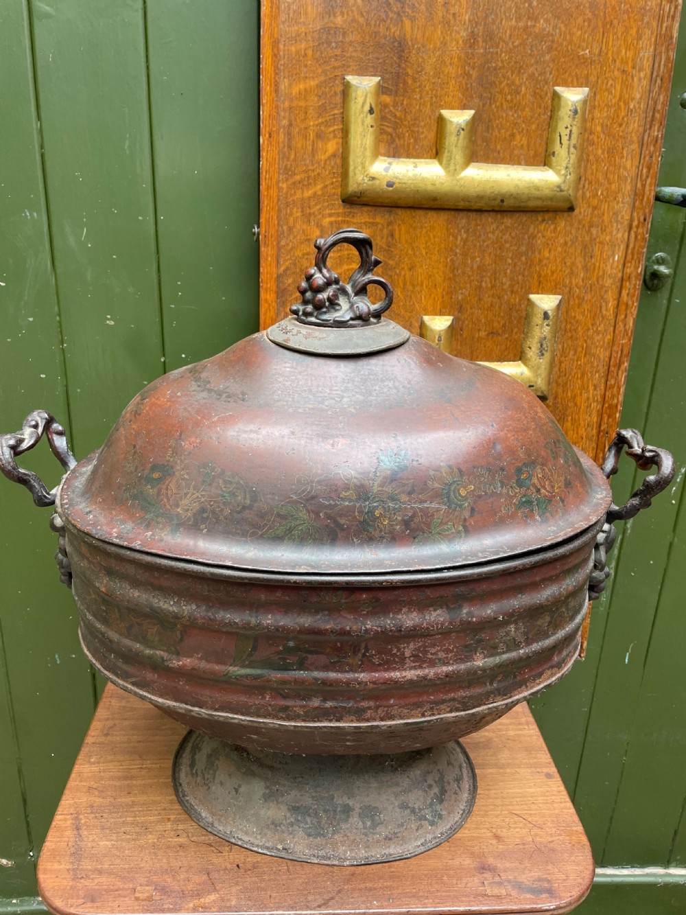 An early nineteenth-century round japanned tinware wine cooler with a domed lid, pedestal base, twin loop handles, and faded painted floral motifs. View XIX