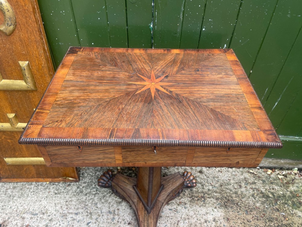 An early nineteenth-century George IV rosewood work table featuring a star-inlaid top, a single drawer casing, a tapered reeded column, and a tripartite base supported by carved claw feet. View XXVII
