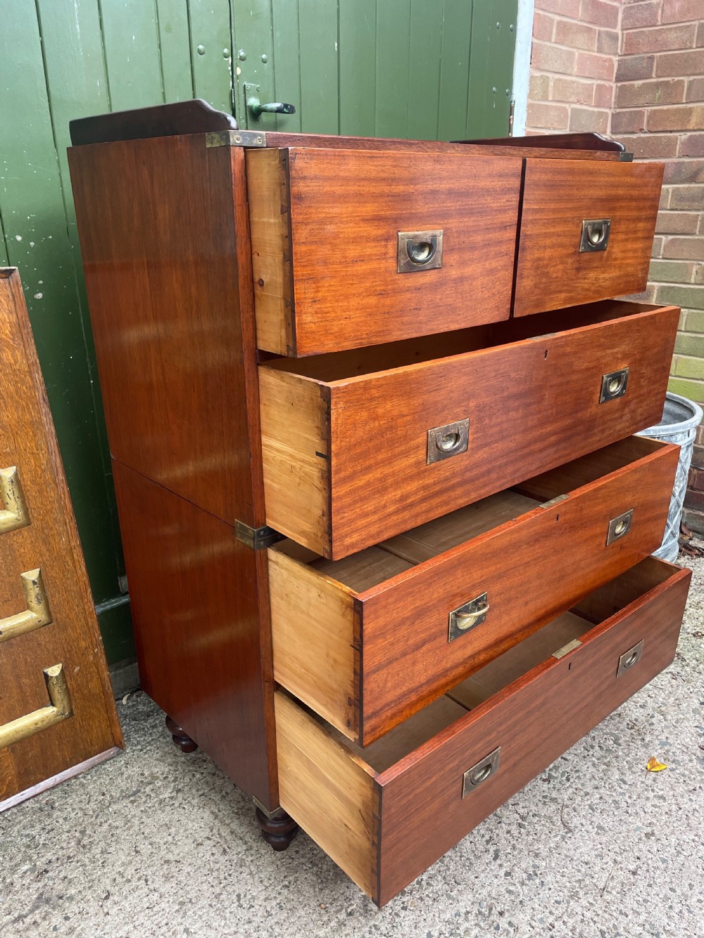 A mid-nineteenth century brass-bound teak campaign chest of drawers featuring two-part construction, recessed brass handles, corner straps, and turned feet. View V