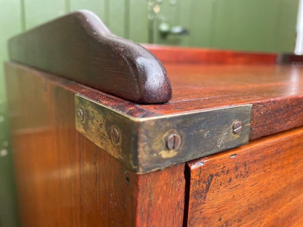A mid-nineteenth century brass-bound teak campaign chest of drawers featuring two-part construction, recessed brass handles, corner straps, and turned feet. View VI