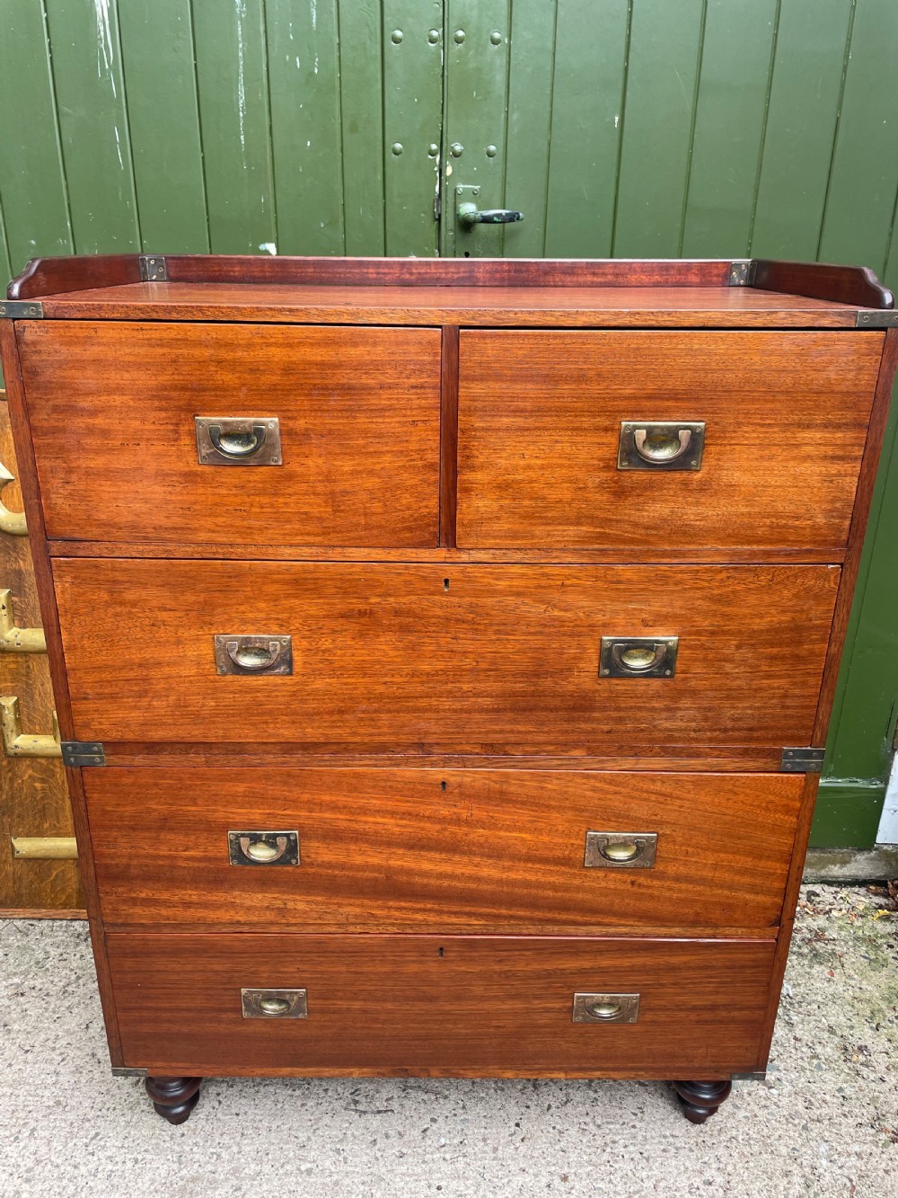 A mid-nineteenth century brass-bound teak campaign chest of drawers featuring two-part construction, recessed brass handles, corner straps, and turned feet. View XVII
