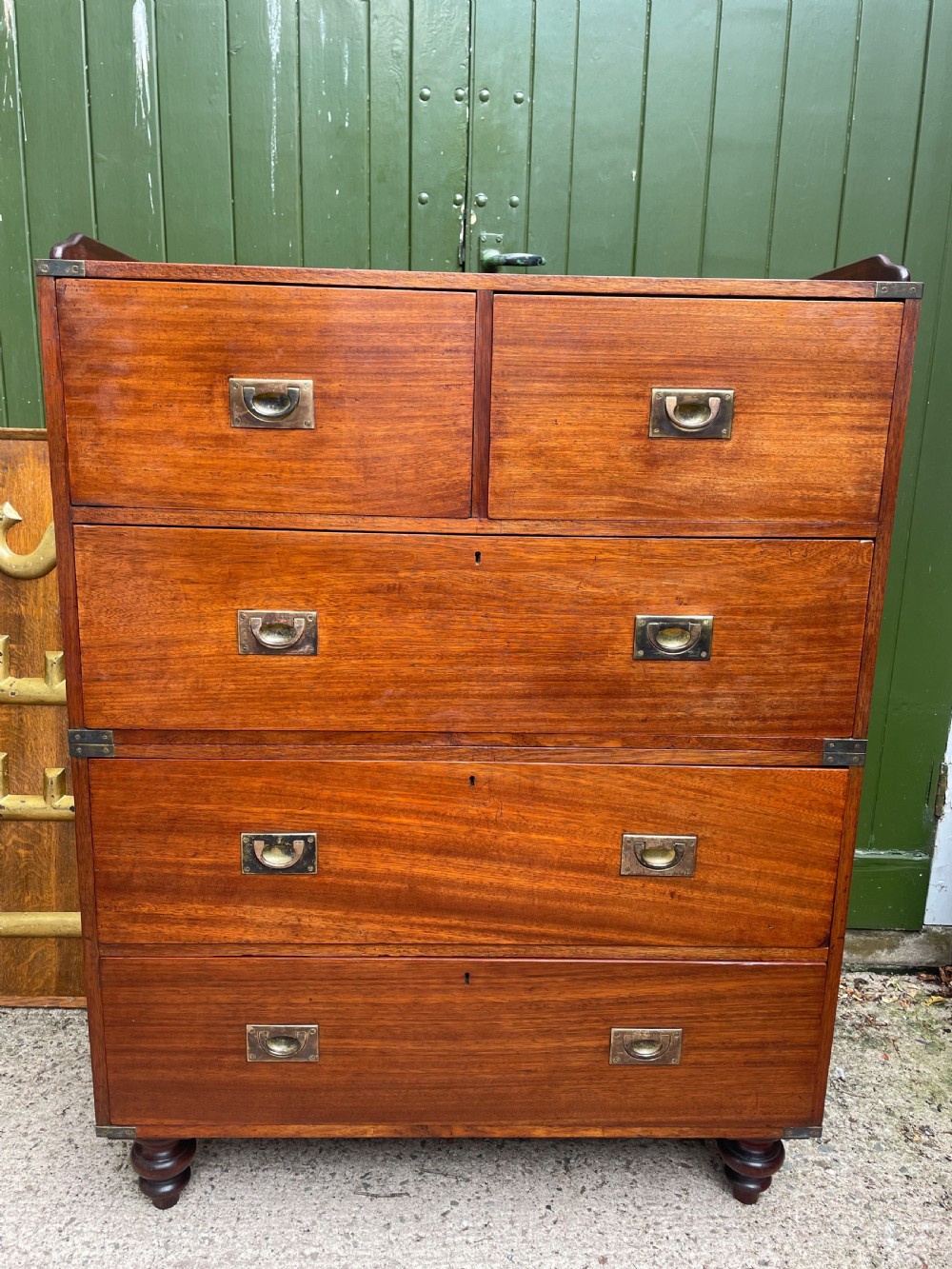 A mid-nineteenth century brass-bound teak campaign chest of drawers featuring two-part construction, recessed brass handles, corner straps, and turned feet. View XVIII