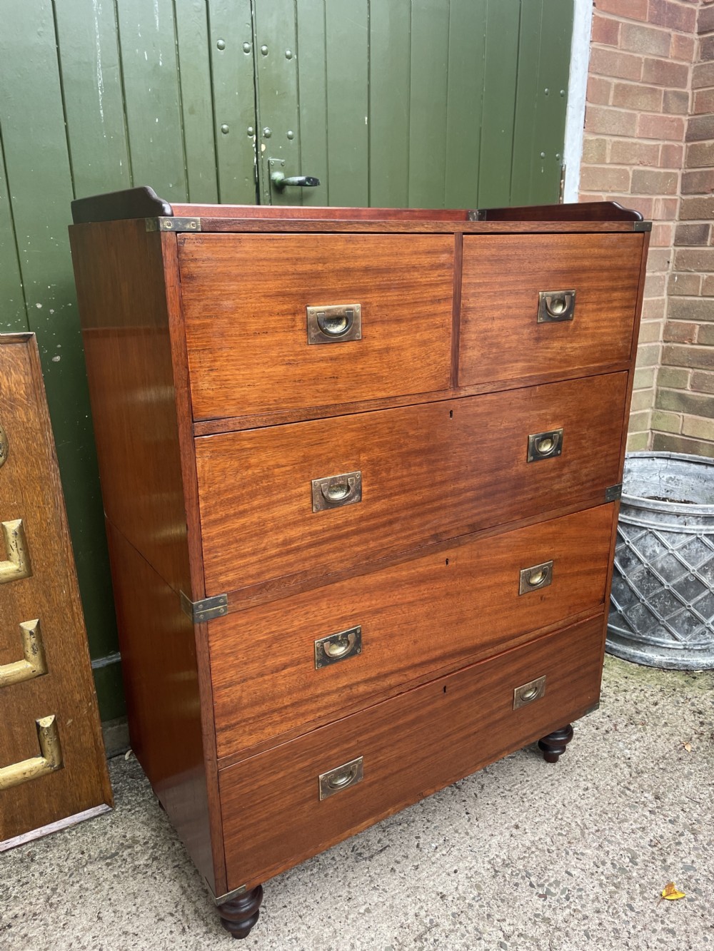 A mid-nineteenth century brass-bound teak campaign chest of drawers featuring two-part construction, recessed brass handles, corner straps, and turned feet. View II