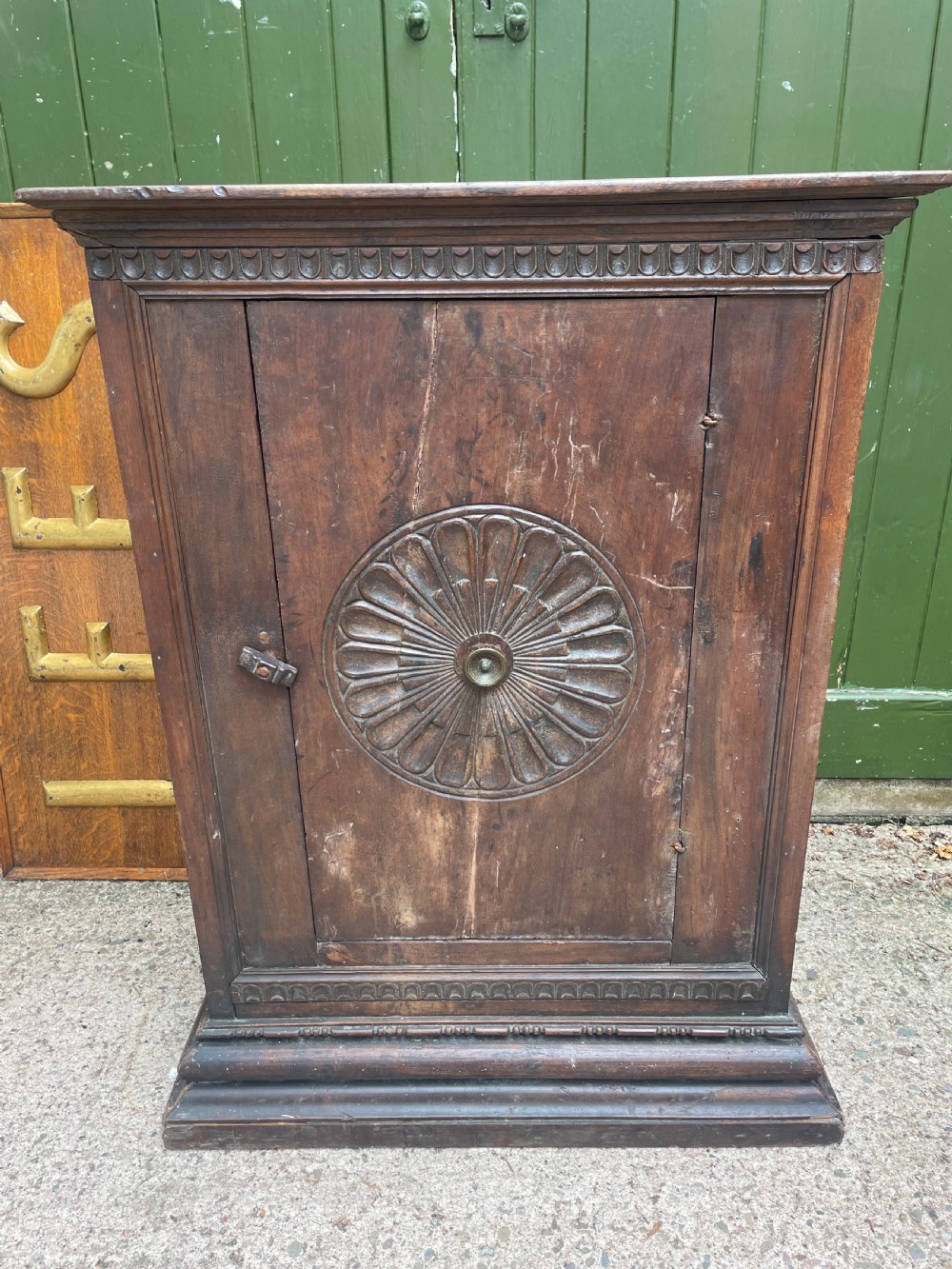 An early 18th-century Italian Tuscan walnut pedestal cupboard featuring a single cupboard door carved with a central circular rosette motif and framed by architectural moulding on a plinth base.