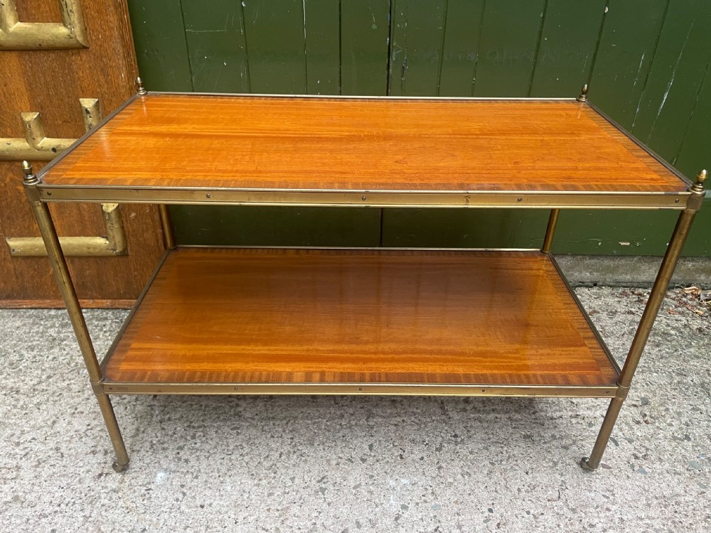 A low rectangular two-tier etagere table featuring satinwood shelves with decorative crossbanded inlay and a brass frame on castors.