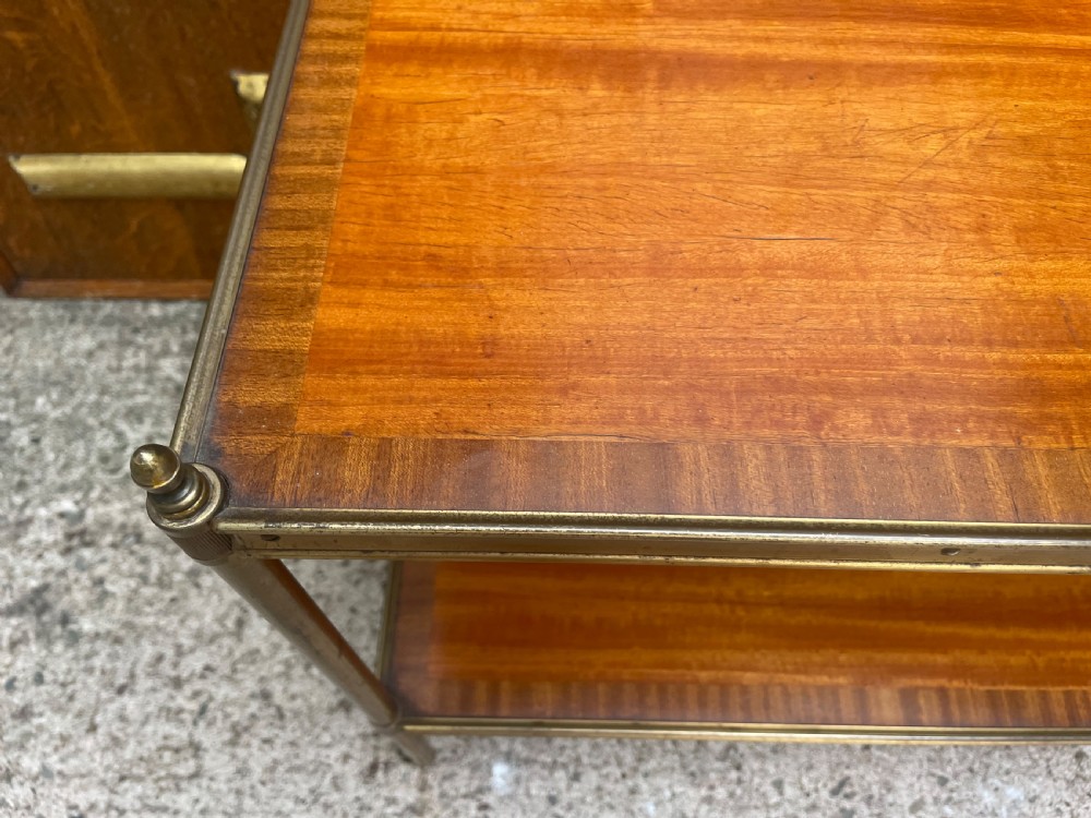 A low rectangular two-tier etagere table featuring satinwood shelves with decorative crossbanded inlay and a brass frame on castors. View II
