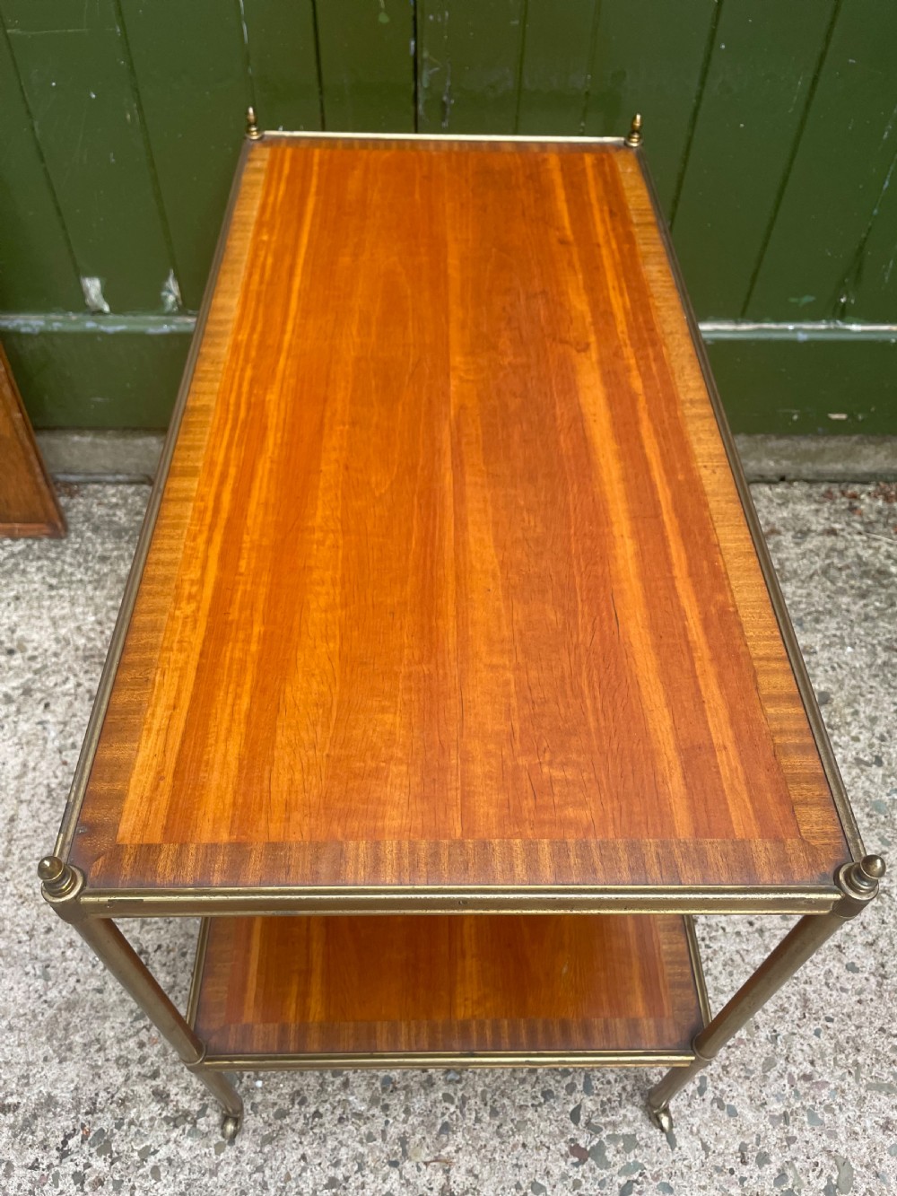 A low rectangular two-tier etagere table featuring satinwood shelves with decorative crossbanded inlay and a brass frame on castors. View VI